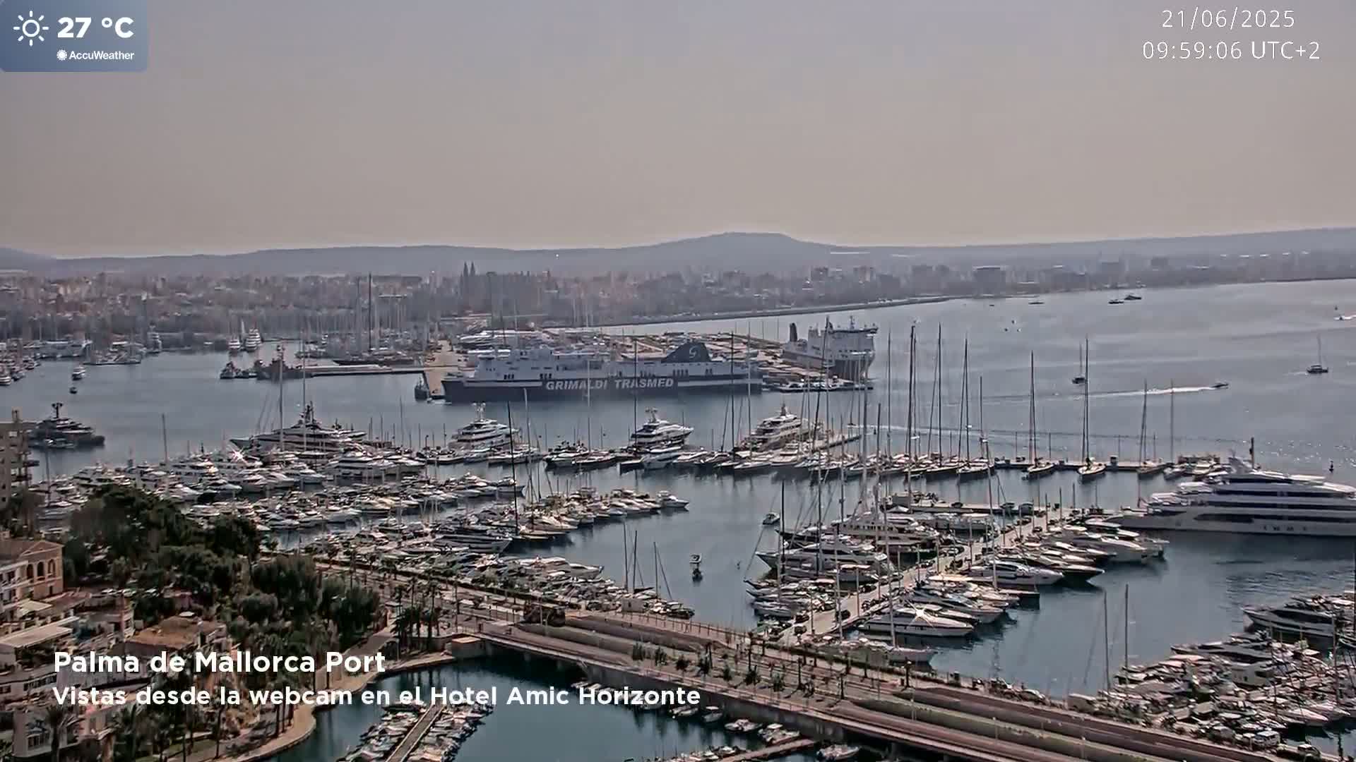 A harbor filled with numerous yachts and sailboats on a hazy, sunny day with a large ferry docked nearby.