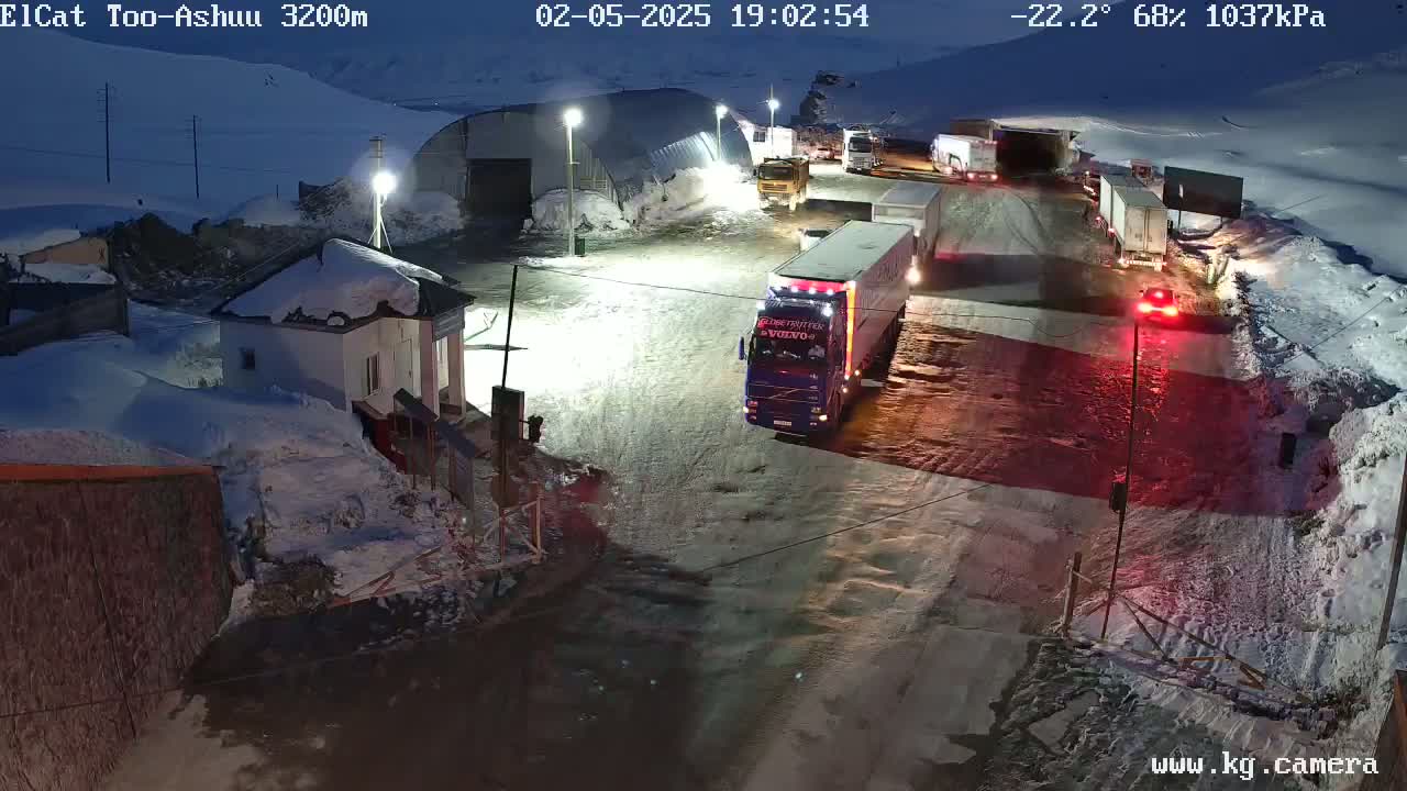 A snow-covered roadway at night with several trucks and buildings, under a dark sky.