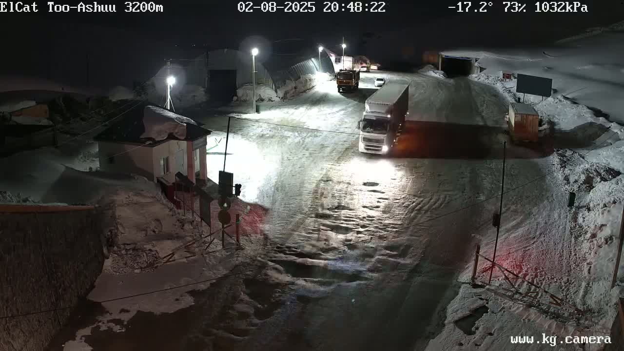 A snow-covered road at night with several trucks and a small building, under conditions of -17.2°C, 73% humidity, and 1032 kPa air pressure.