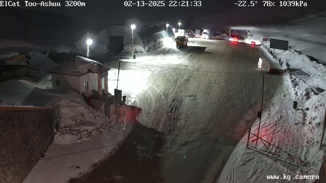 A snow-covered road at night with several vehicles and a building, under a dark sky with a temperature of -22.5 degrees Celsius and 78% humidity.