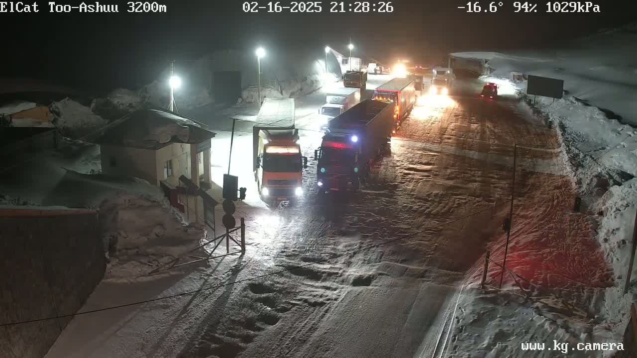 A nighttime, snowy scene shows several large trucks stopped on a road near a building, with the temperature at -16.6 degrees.