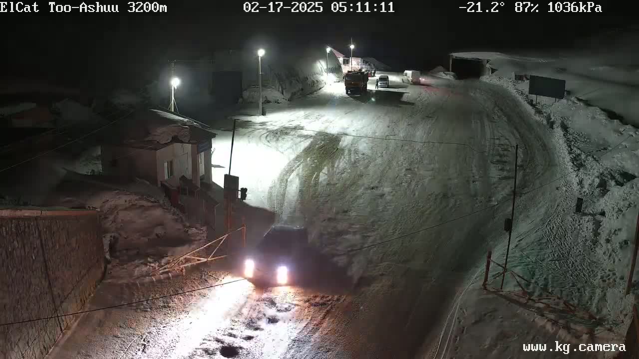 A snow-covered road at night with several vehicles, including a truck, is illuminated by streetlights.