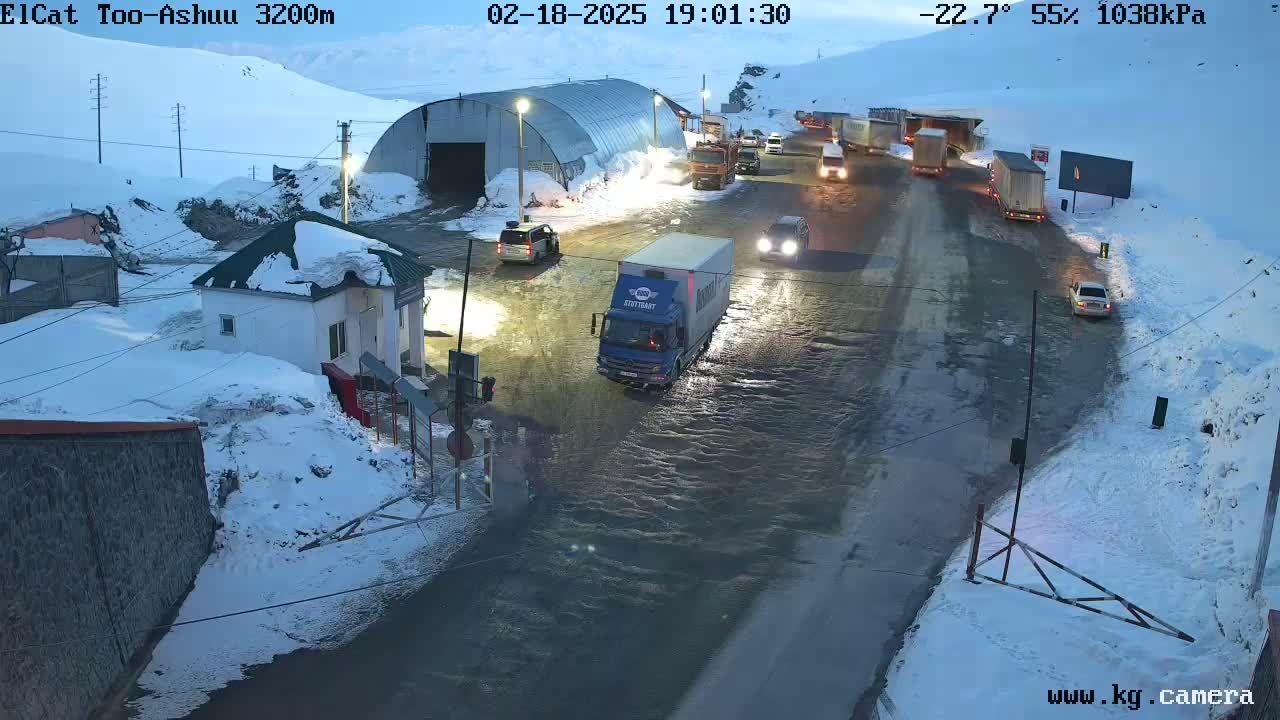 A snow-covered roadway with several vehicles, including a truck, is partially flooded under a twilight sky.