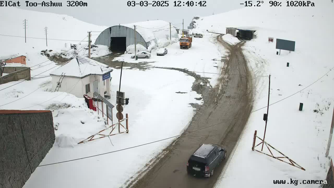 A snow-covered mountain road scene shows several vehicles near a small building and a tunnel entrance, with a dark-colored SUV in the foreground.