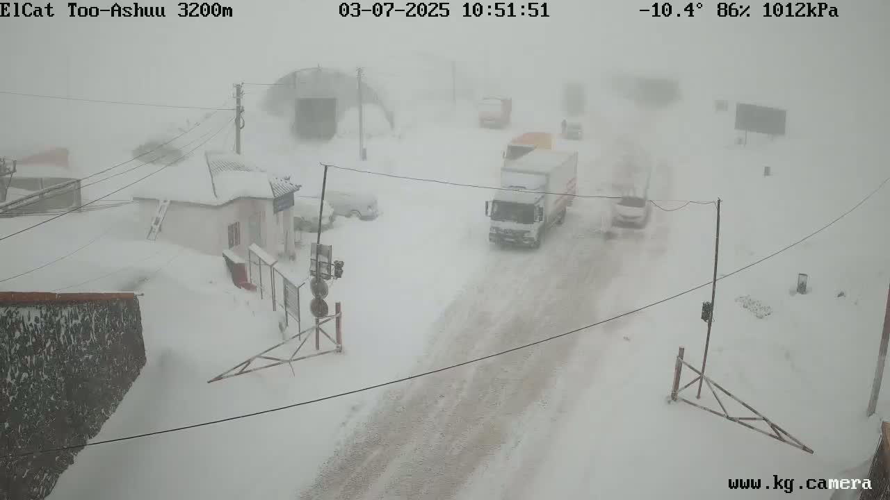 A snow-covered road with several vehicles driving through a heavy snowstorm.