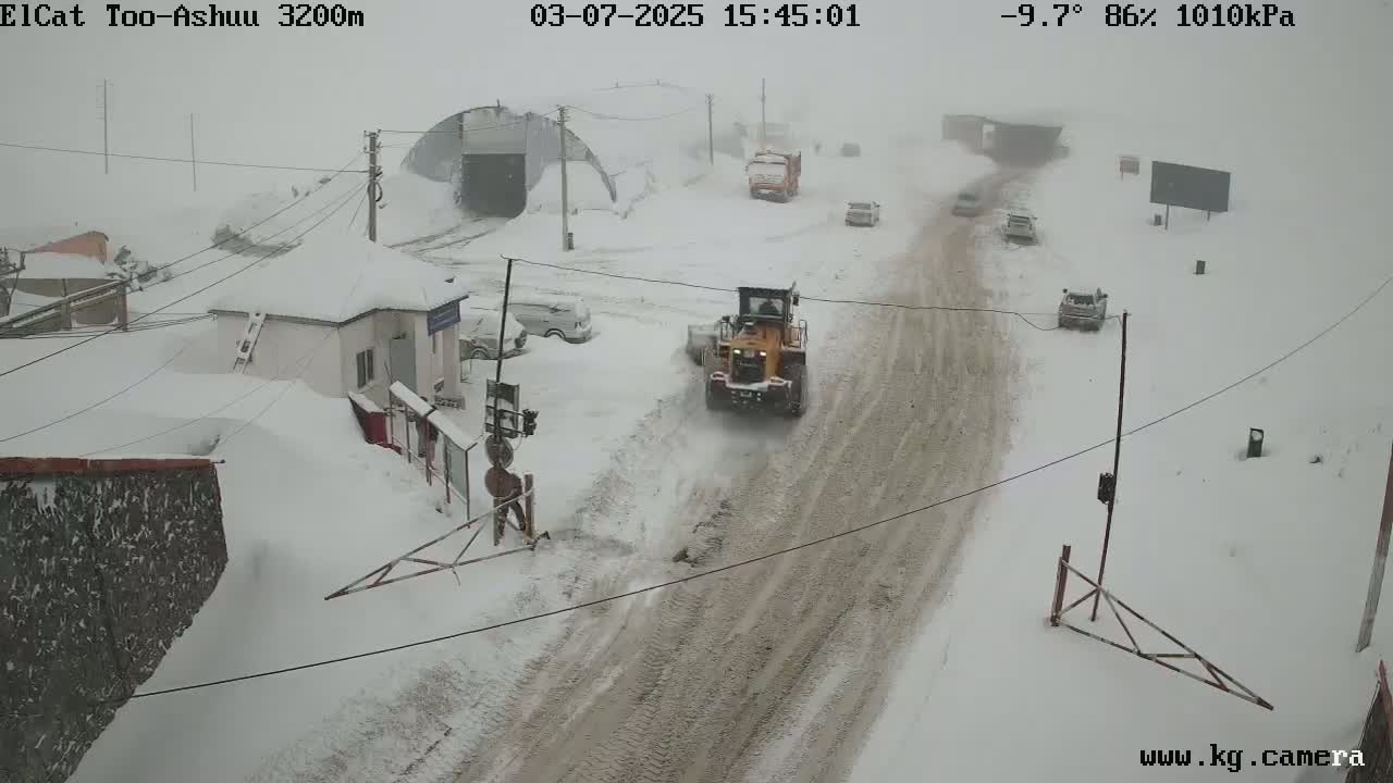 A snow-covered road with several vehicles and a snowplow is visible in a heavy snowstorm.