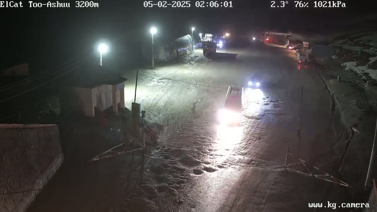 Several vehicles are traveling on a wet, dark road at night, illuminated by streetlights.