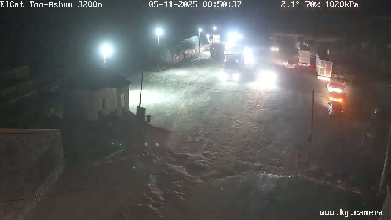 At night, under a 70% humidity and 2.1°C temperature, several vehicles are seen driving on a wet, dimly lit road near a building.