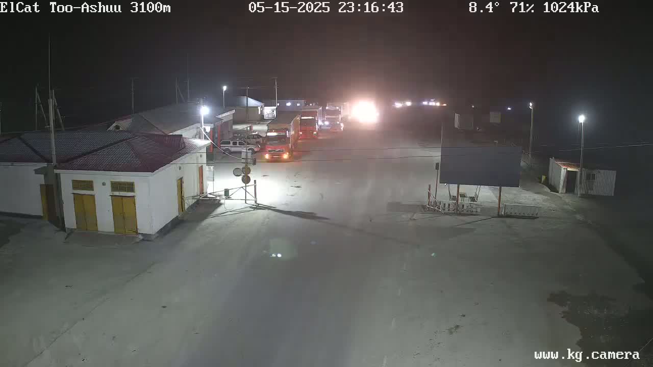 At night, under a clear sky with a temperature of 8.4 degrees and 71% humidity, several semi-trucks are parked in a lot near a small building.
