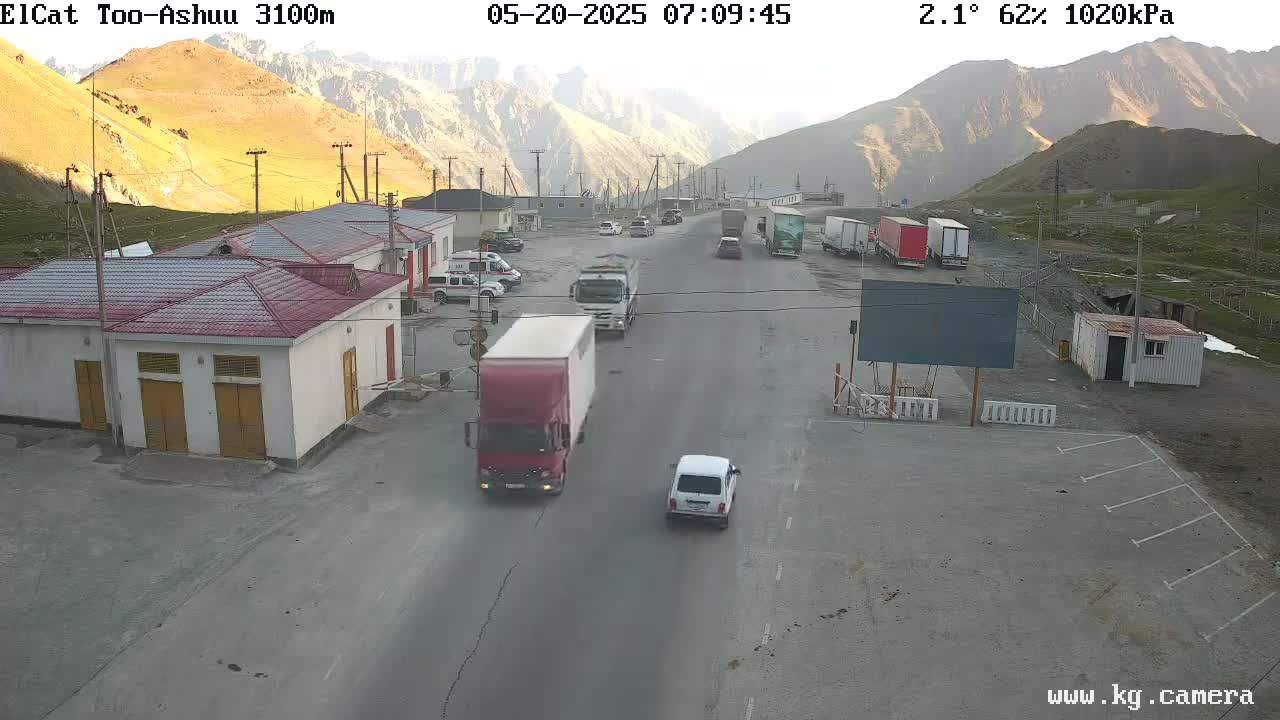 A mountain pass border crossing with several vehicles, including trucks and cars, on a sunny day.
