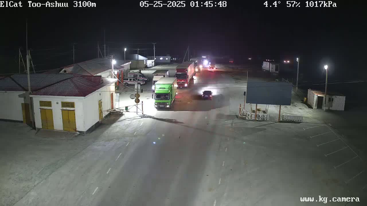 At night, under a clear sky with a temperature of 4.4°C and 57% humidity, several vehicles, including trucks and cars, are seen in a dimly lit area near buildings.