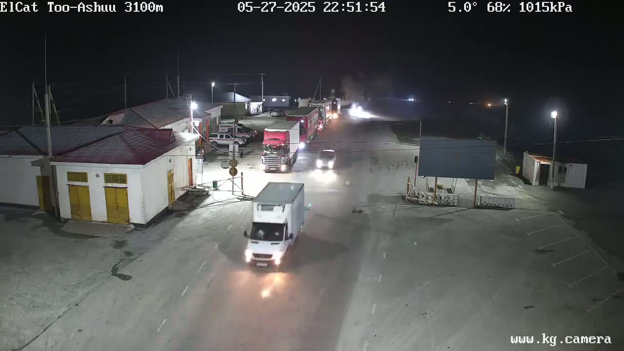 A nighttime scene shows several trucks and cars moving along a road near buildings under a 5°C temperature with 68% humidity.