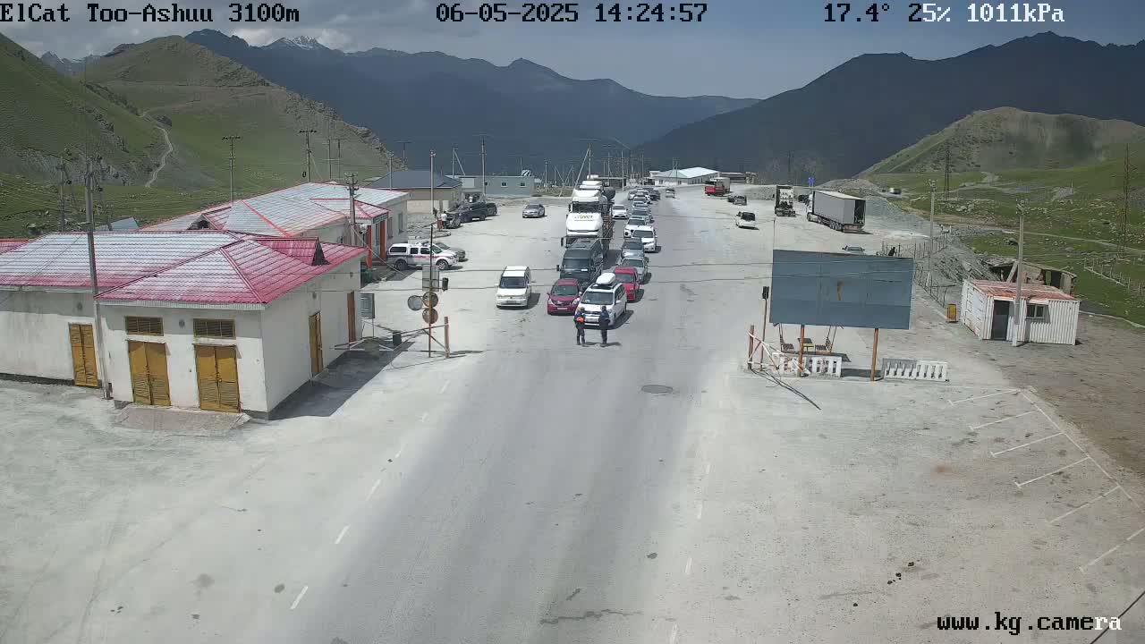 A mountain pass checkpoint with several vehicles waiting, under a sunny sky with a temperature of 17.4 degrees Celsius and 25% humidity.