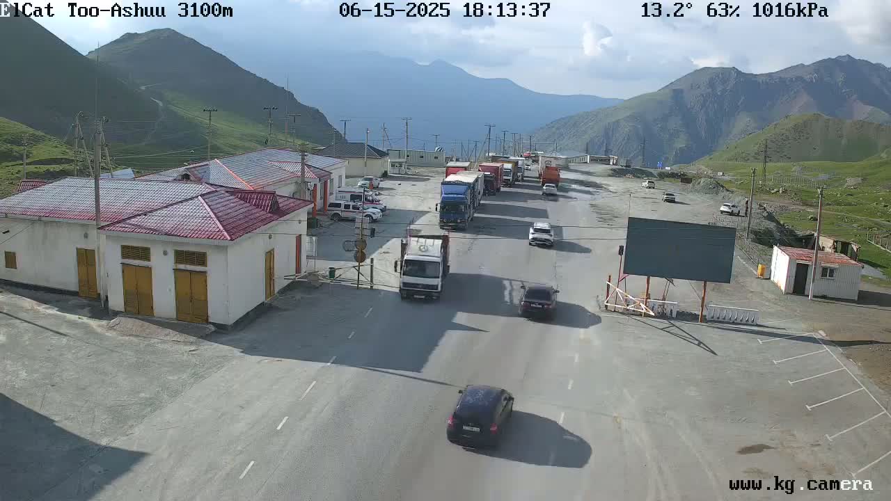 A mountain pass border crossing with several vehicles, including trucks and cars, on a partly cloudy day.
