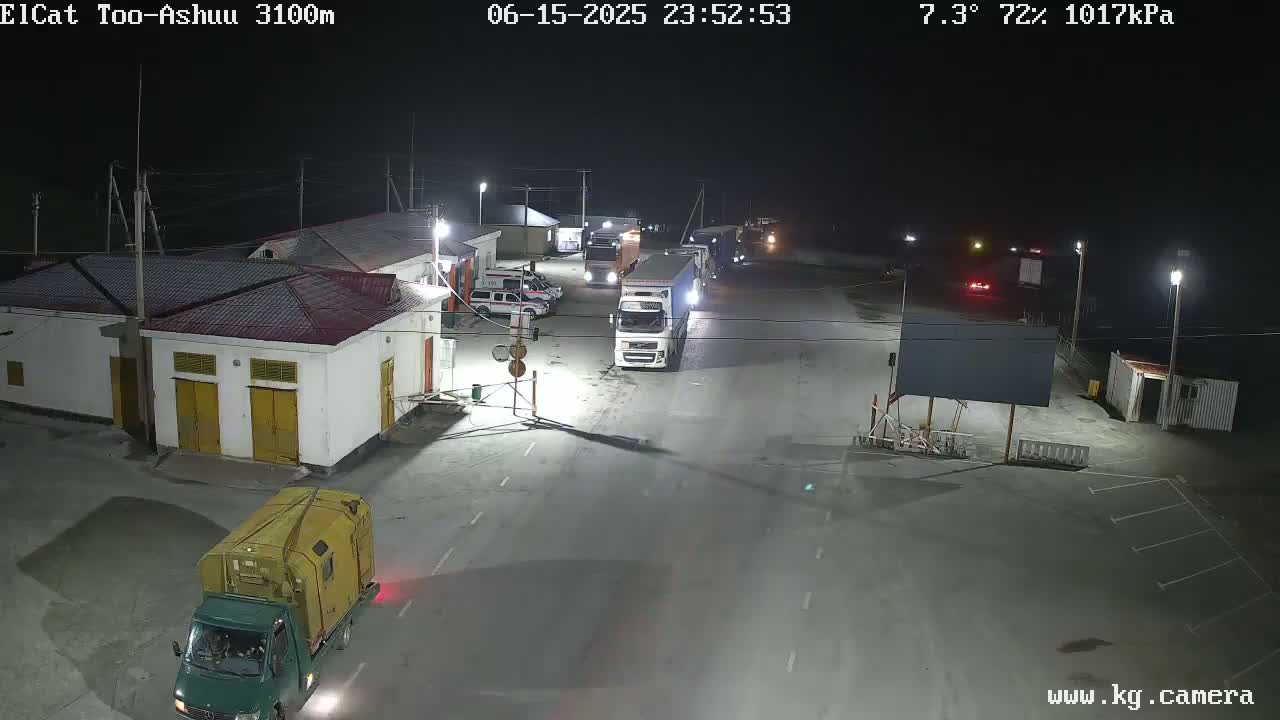 A nighttime, outdoor view of a roadway with several trucks and other vehicles parked or stopped at what appears to be a border crossing or checkpoint, under a clear sky.