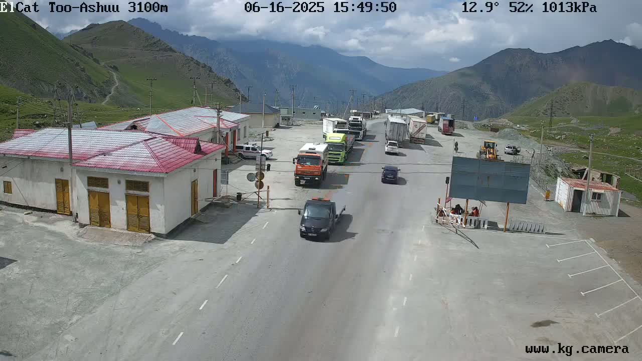 A mountain pass checkpoint with several trucks and cars parked along a road on a partly cloudy day.