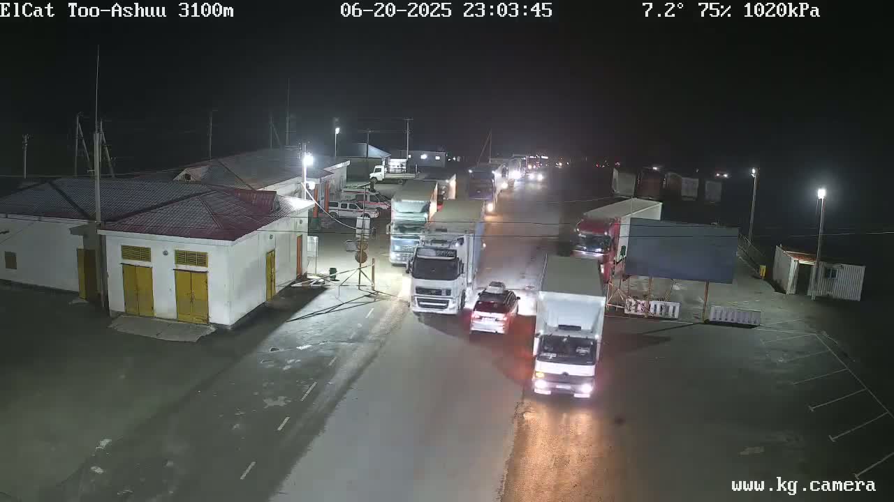 At night, several trucks and cars are stopped on a roadway in front of buildings under a clear sky with a temperature of 7.2 degrees and 75% humidity.