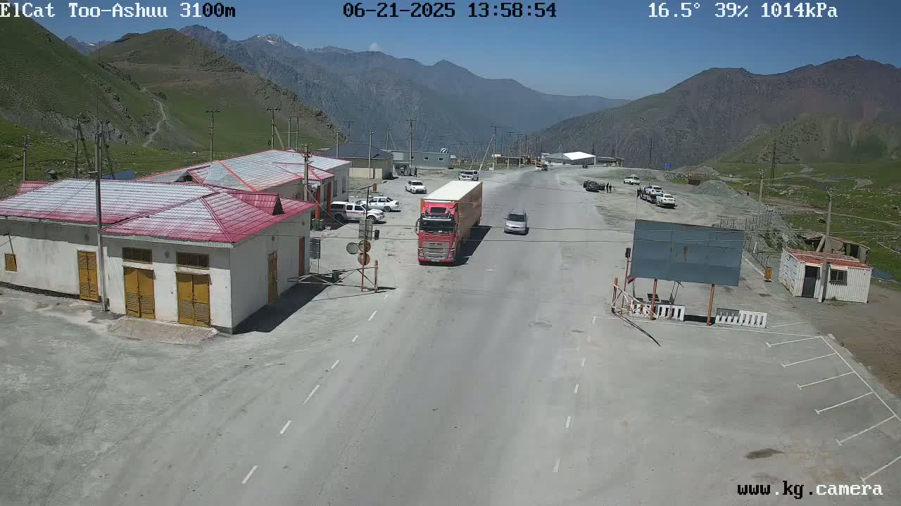 A highway checkpoint in a mountainous area on a sunny day with several vehicles parked and a truck driving through.