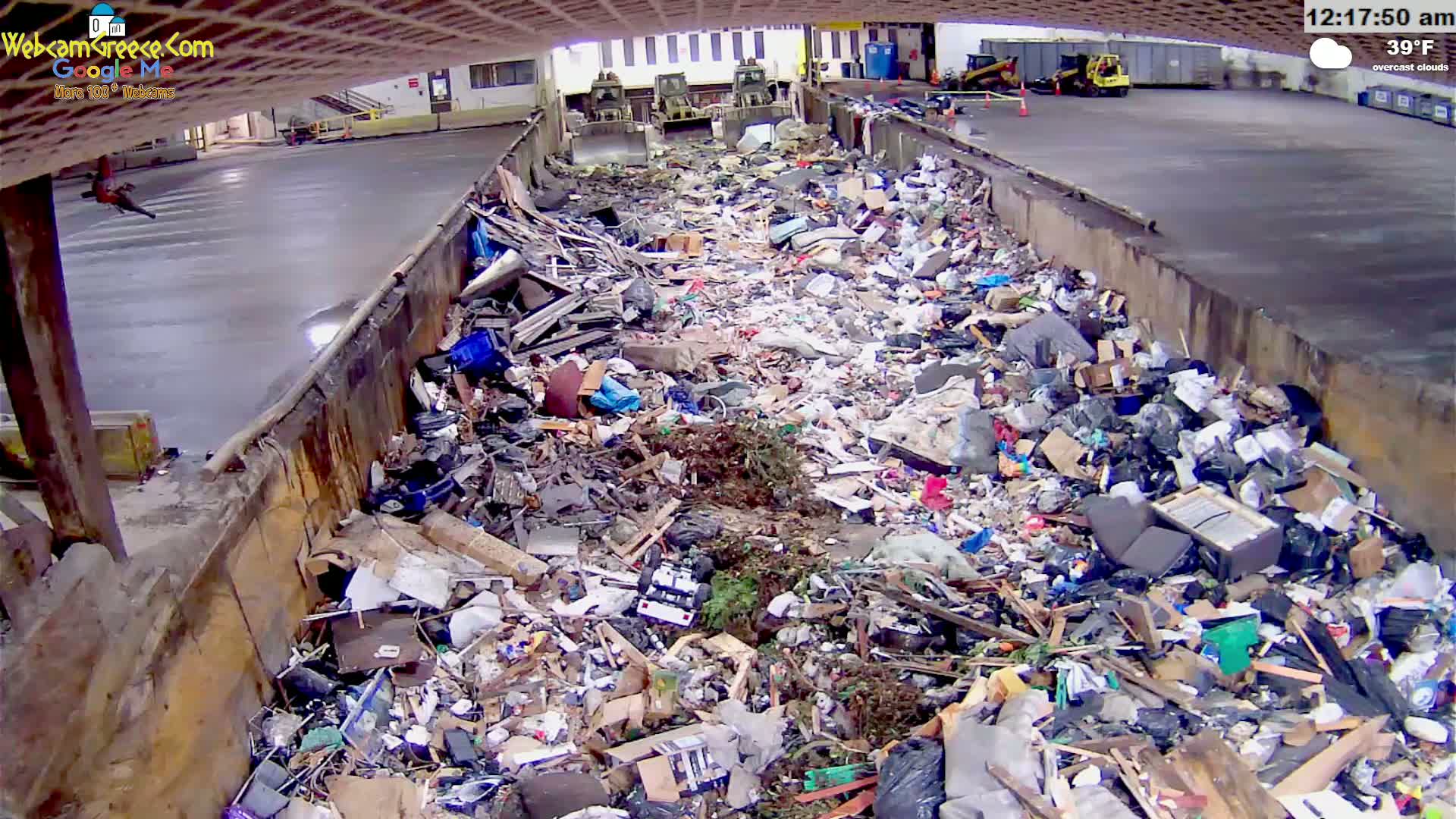 A large pile of refuse sits in an outdoor, overcast, concrete-walled enclosure at 39°F.