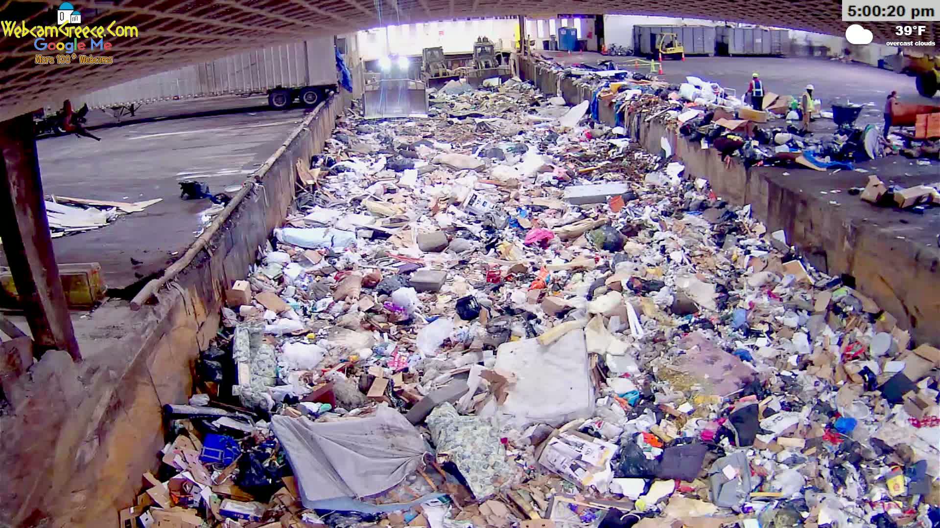 A large pile of refuse sits under an overcast sky at 39°F in an open-air structure.