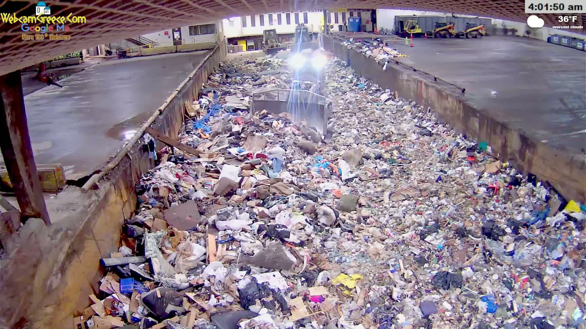 A large pile of trash is being compacted by machinery in an indoor facility under overcast skies at 36°F.