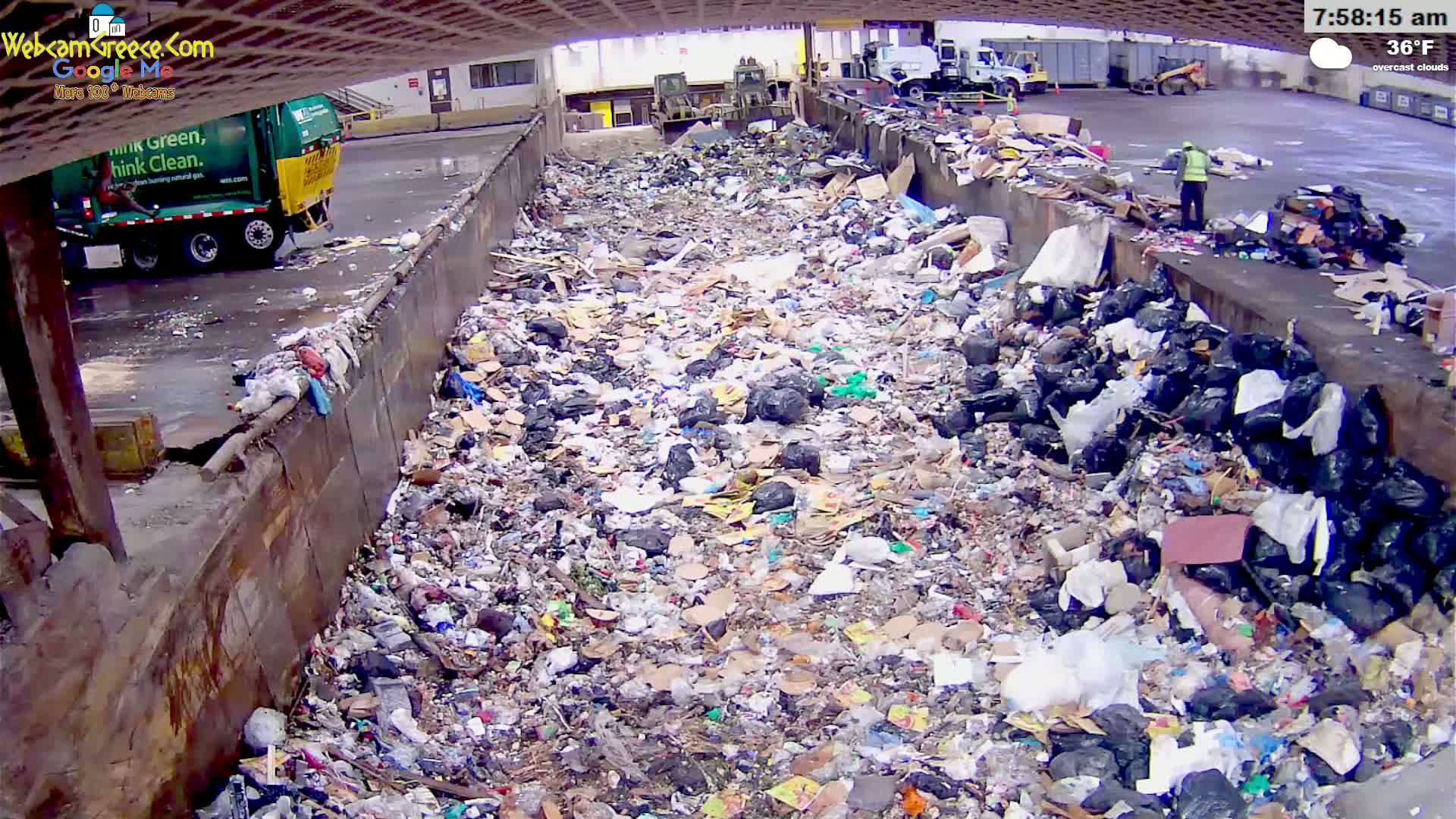 A large pile of garbage sits in an outdoor waste receptacle under overcast skies.