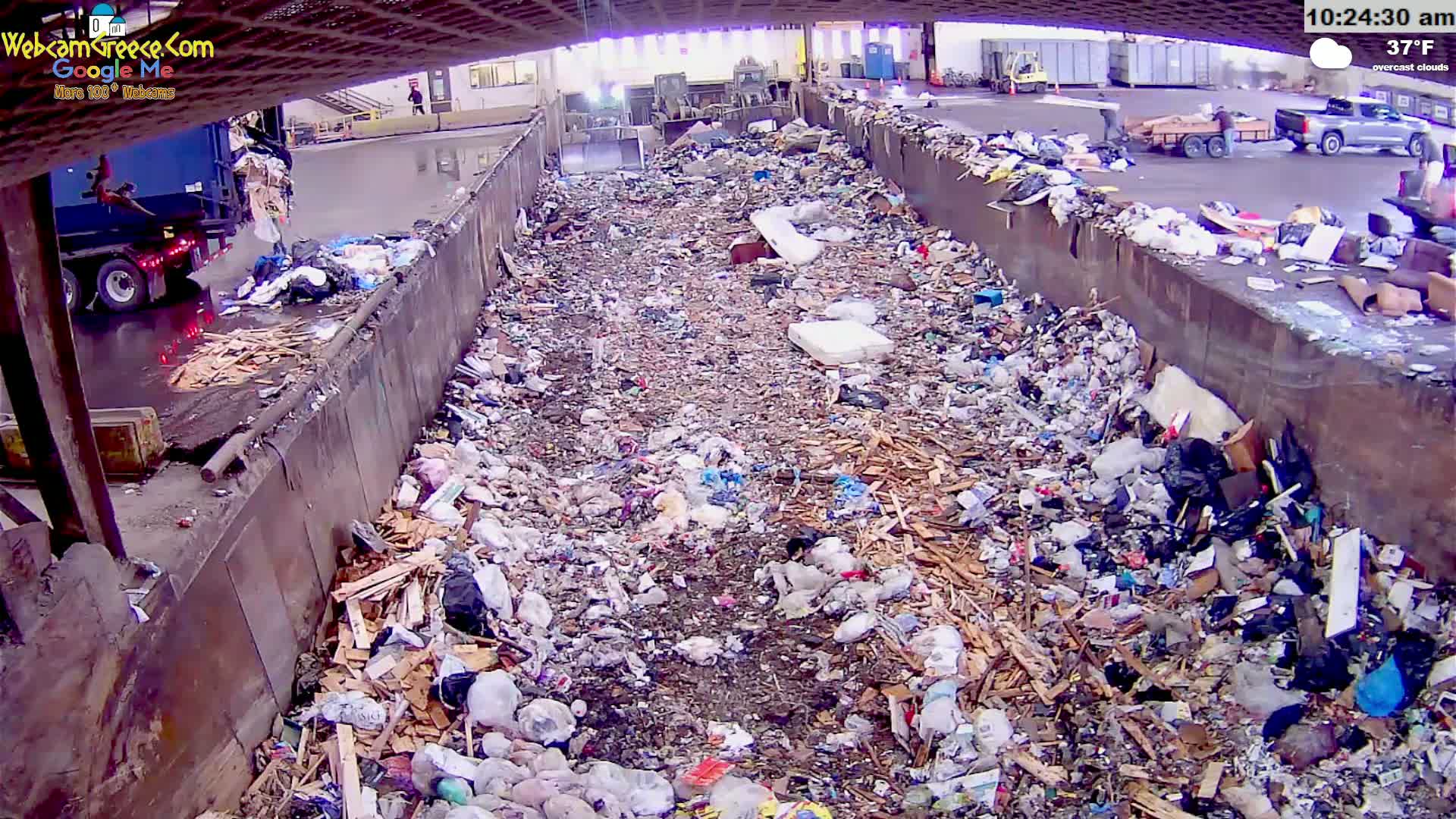 A large pile of trash and wood scraps fills a long, concrete-walled trough outdoors on an overcast day at 37°F.