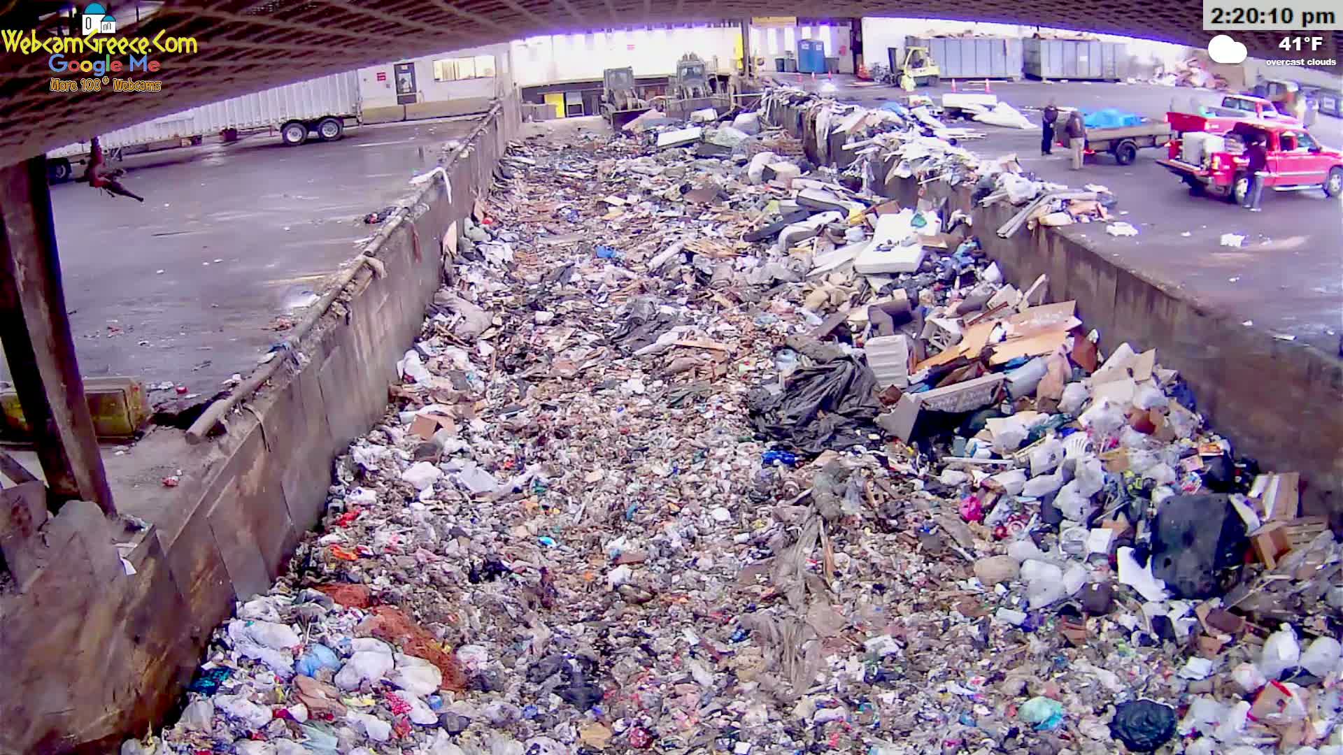 A large pile of trash fills a long, narrow concrete trough outdoors under overcast skies.