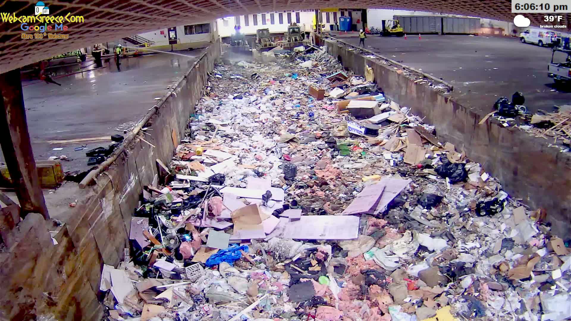 A large amount of trash and debris fills a long, narrow concrete receptacle under broken clouds at 39°F.