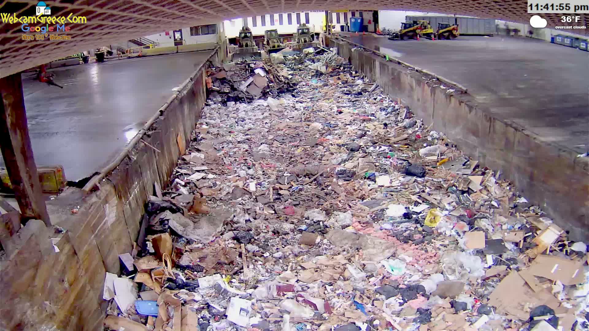 A large pile of trash sits in an outdoor concrete receptacle under overcast skies.