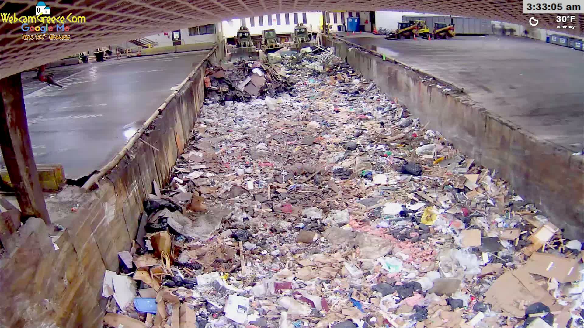 A large pile of trash fills a concrete-walled containment area under a clear sky at 3:33 am.