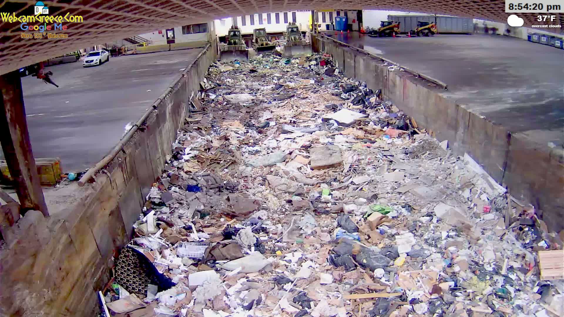 A large amount of garbage and debris fills a long, narrow concrete pit outdoors under overcast skies.