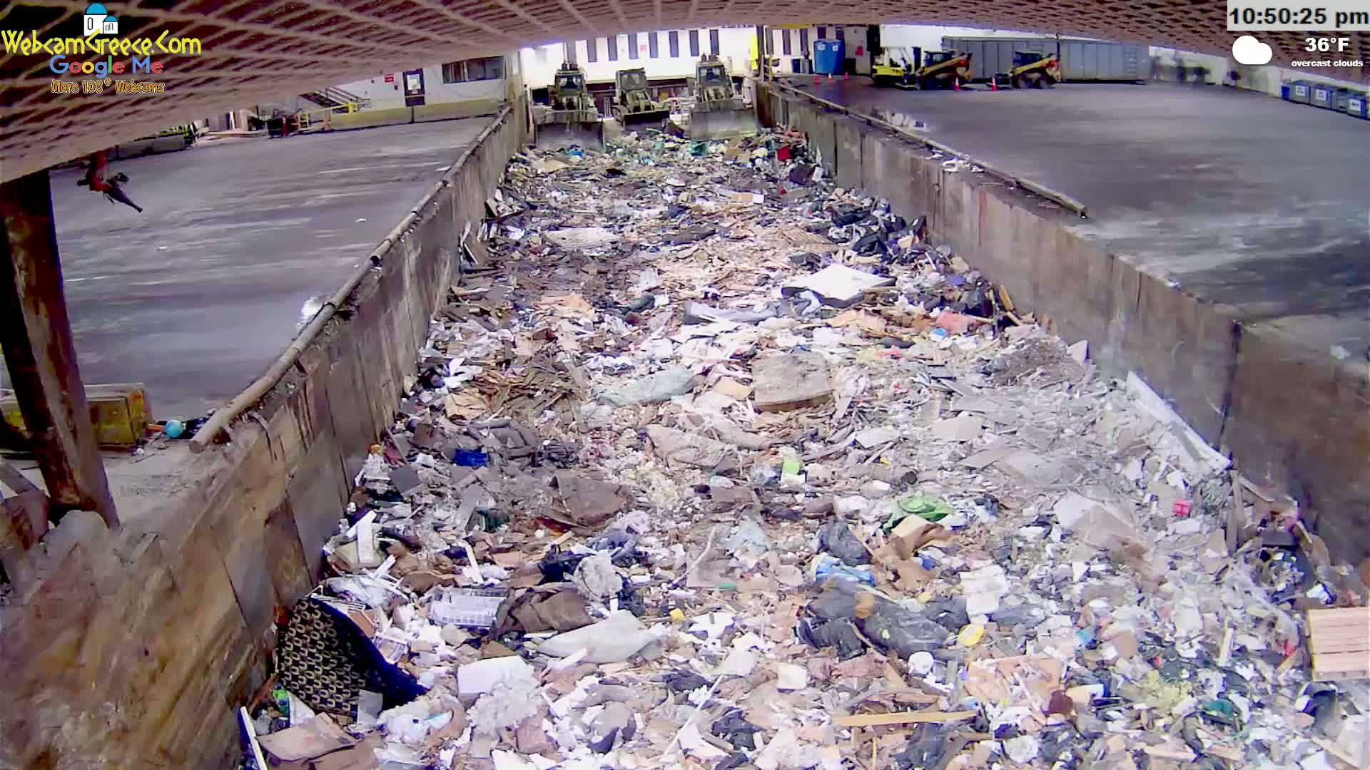 A large pile of trash is seen in an outdoor waste receptacle under overcast skies.