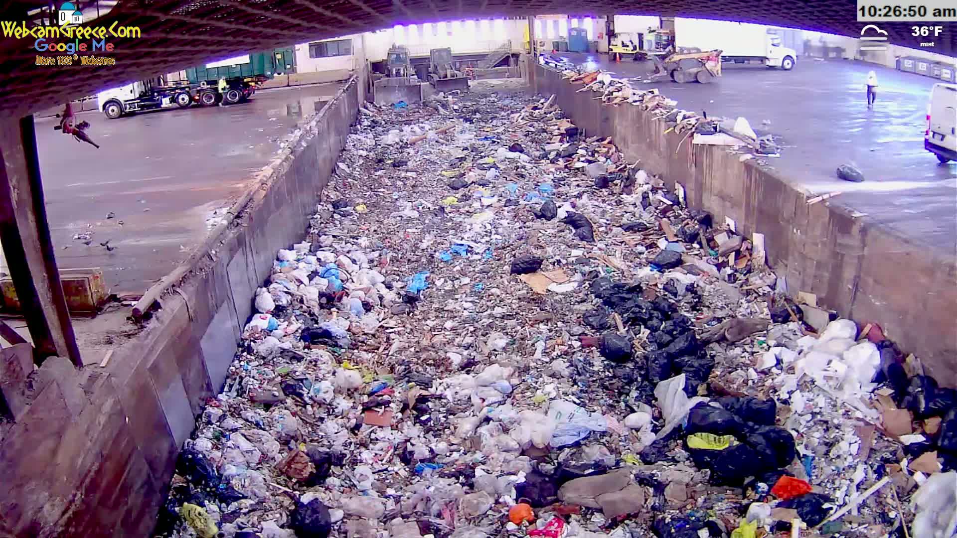 A large pile of trash is accumulating in a concrete-walled chute outdoors in misty, 36°F weather.