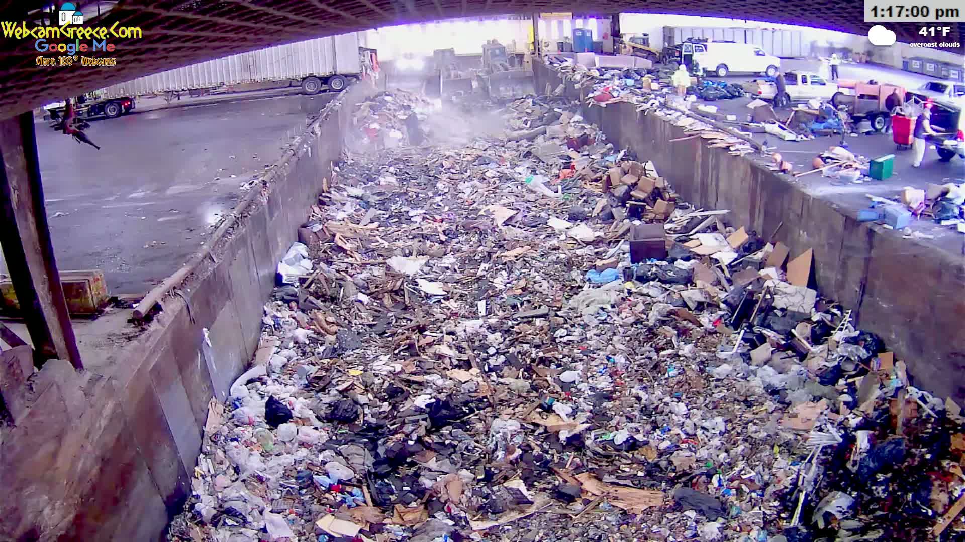 A large pile of garbage fills a concrete-walled pit outdoors under overcast skies.