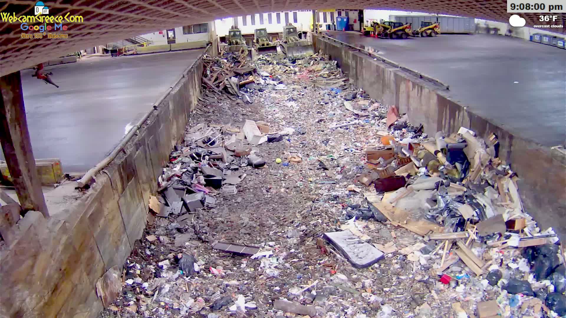 A large amount of trash and debris is piled in a long, narrow, concrete-walled trench under an overcast sky at 36°F.