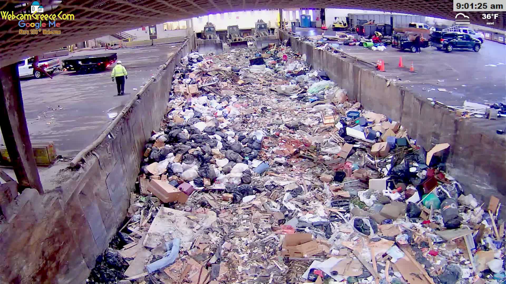A large amount of trash and debris is piled high inside a concrete structure under a misty sky.