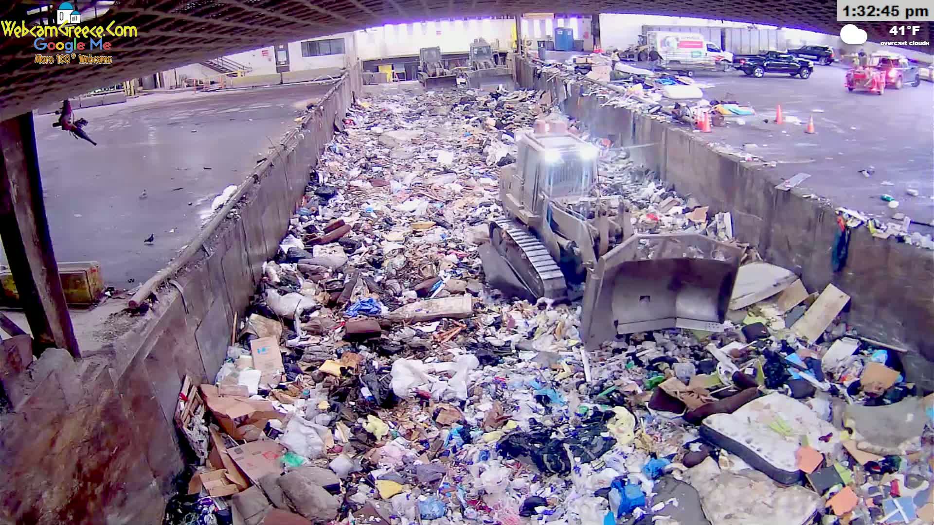 A bulldozer is working within a large landfill filled with various types of trash under overcast skies at 41°F.