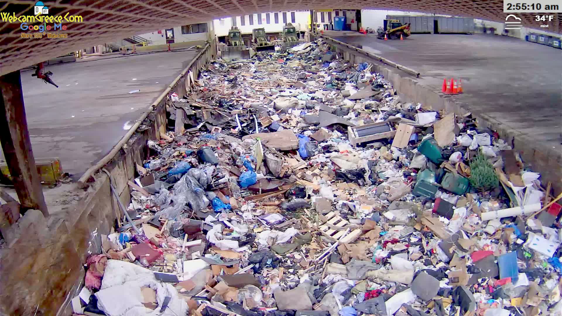 A large pile of trash sits in a concrete pit outdoors in misty 34°F weather.