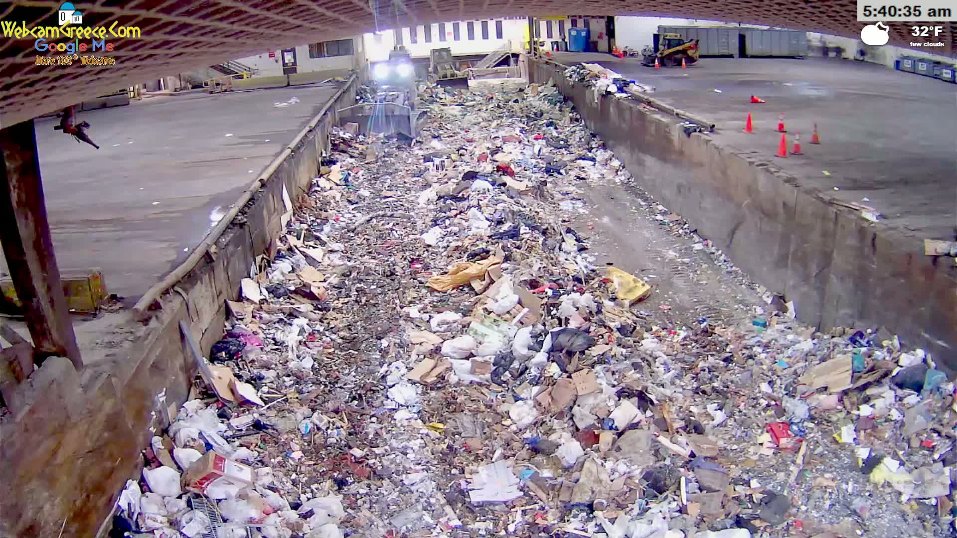 A large amount of trash is piled in a concrete trough under a partly cloudy sky, with a machine working to process it.