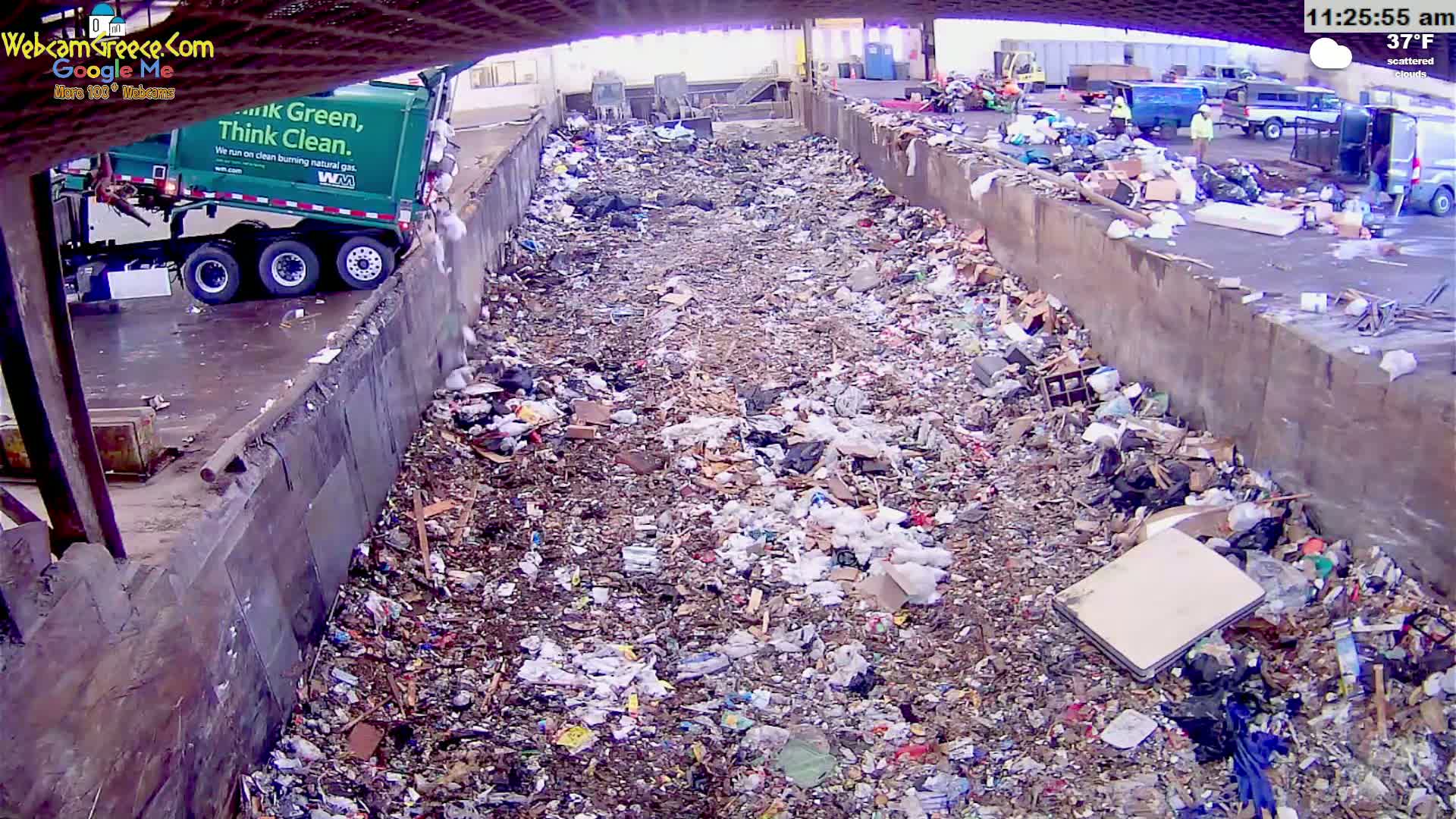 A garbage truck dumps its load into a large, overflowing landfill under scattered clouds and a 37°F temperature.