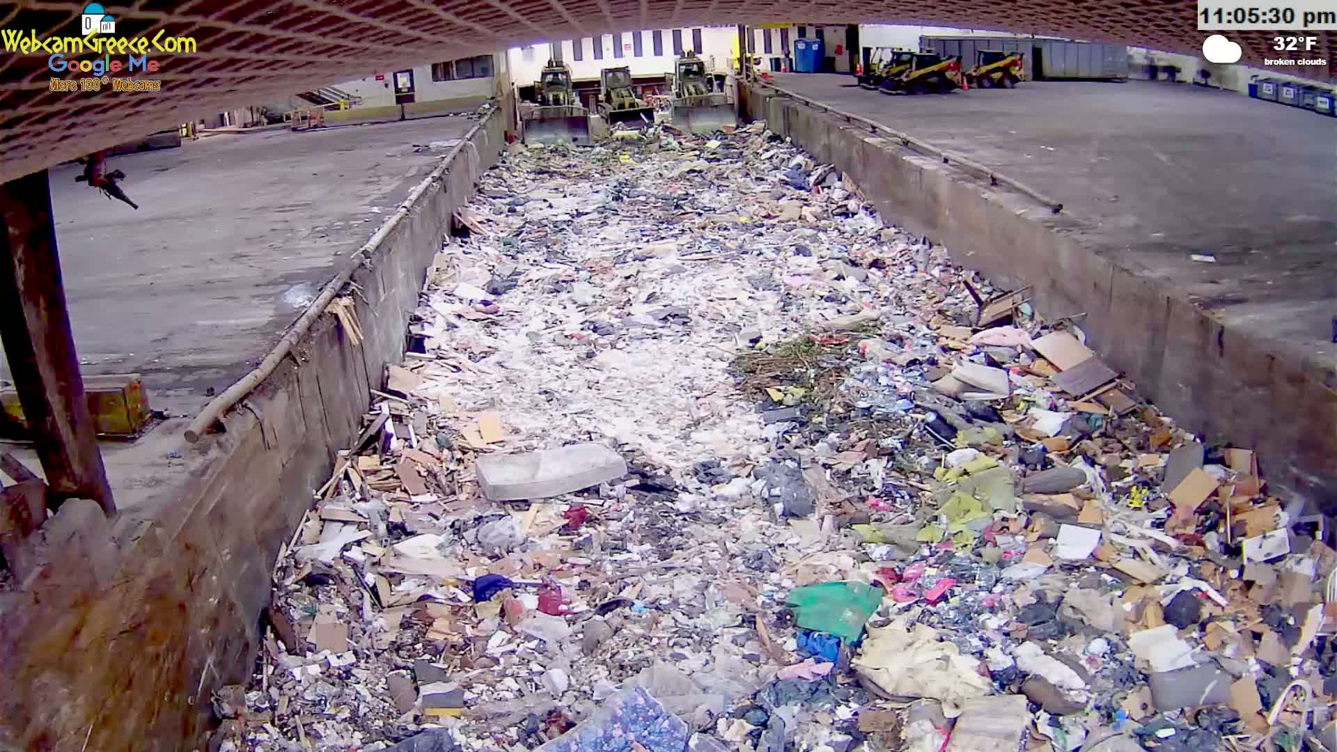 A large pile of refuse fills a long, concrete-walled trough outdoors under broken clouds and a 32°F temperature.