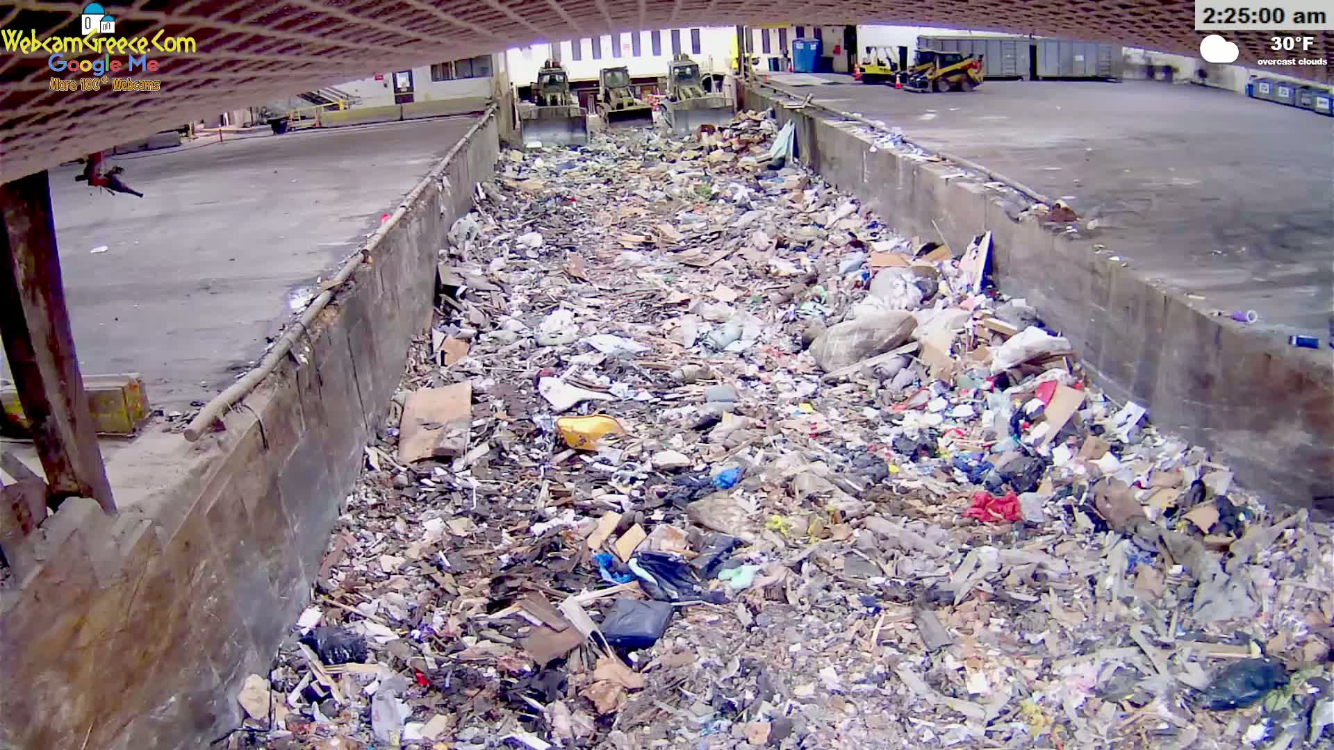 A large pile of trash sits in a concrete trough under overcast skies at 30°F.