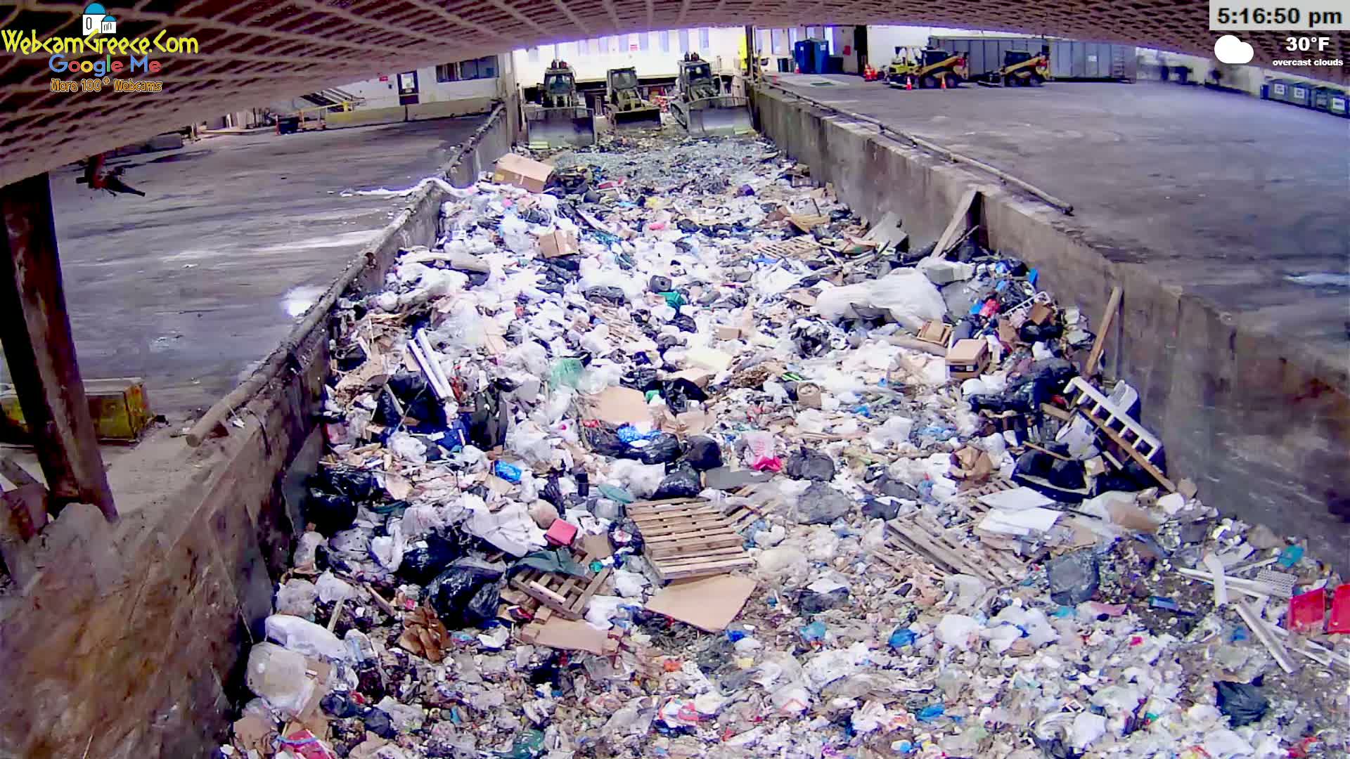 A large pile of trash sits in a concrete-walled pit under overcast skies, with the temperature at 30°F.