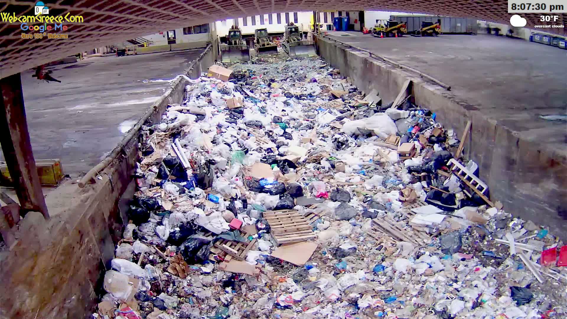 A large pile of garbage is seen in a concrete-walled enclosure under overcast skies at 30°F.