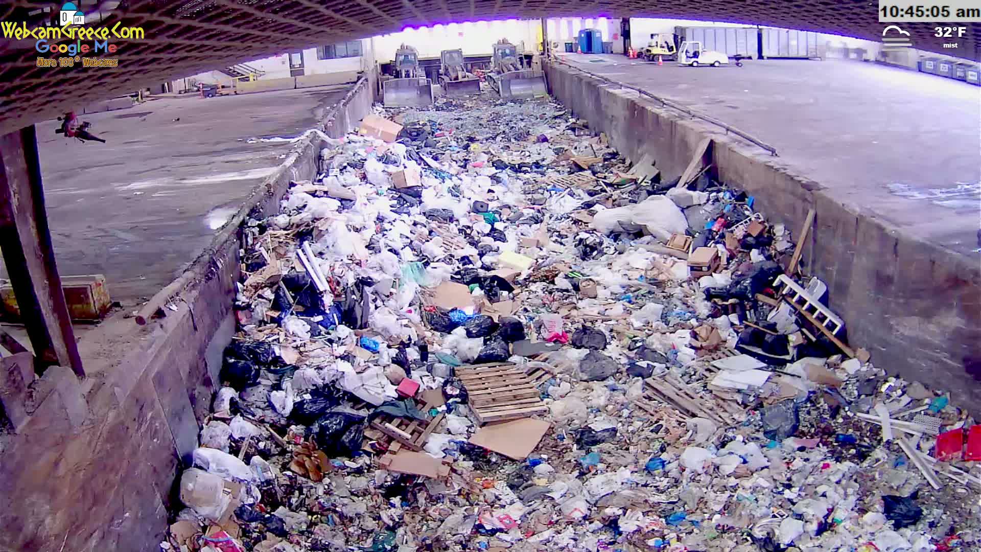 A large pile of trash sits in a concrete trough outdoors in misty, 32°F weather.