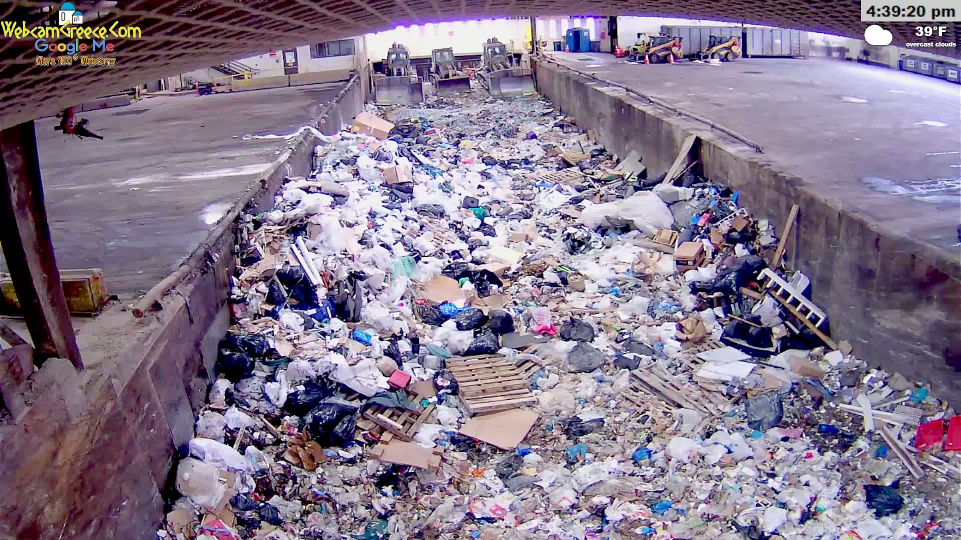 A large pile of garbage sits in a concrete trough under an overcast sky, with the temperature at 39°F.