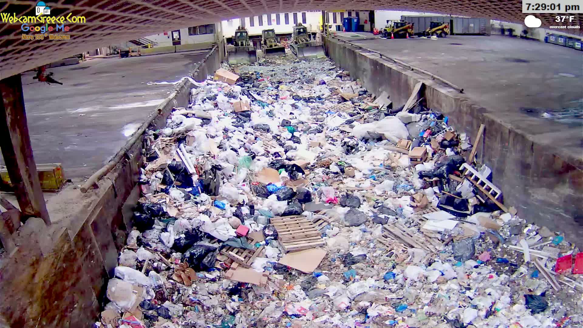 A large pile of garbage fills a concrete trough under overcast skies at 37°F.