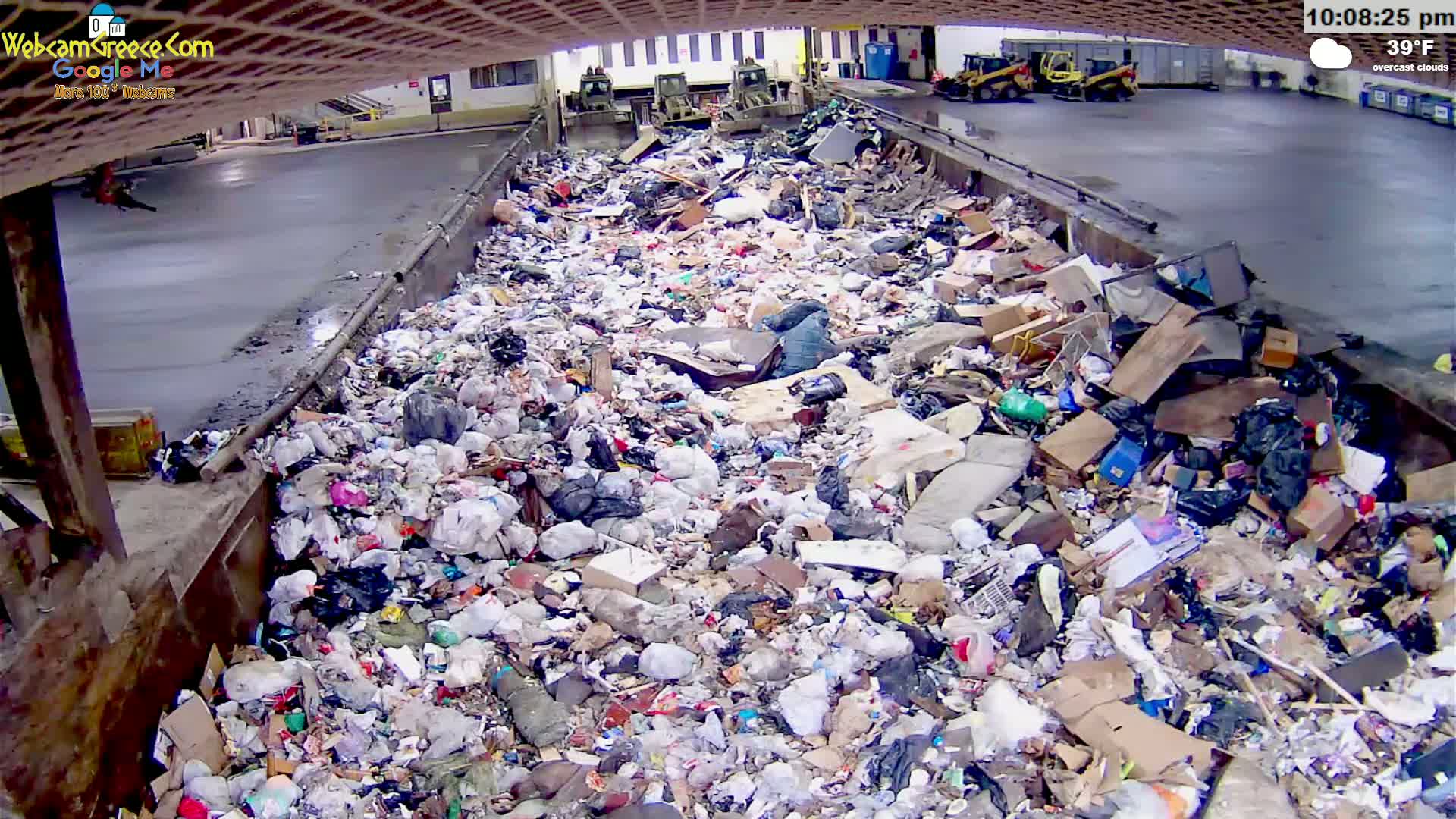 A large amount of garbage is piled in an outdoor container under overcast skies, with the temperature at 39°F.