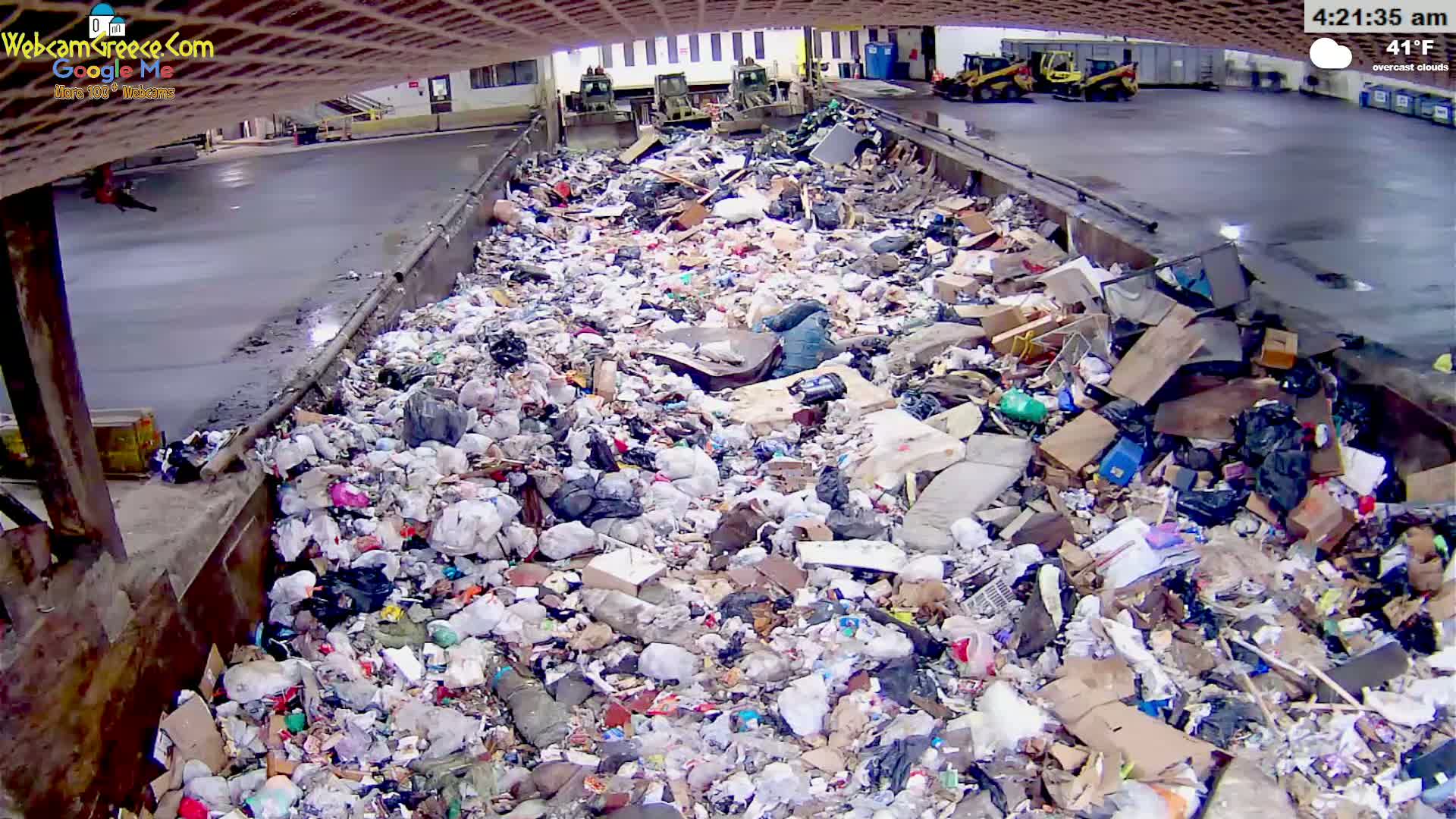 A large pile of garbage sits in a concrete container under overcast skies.